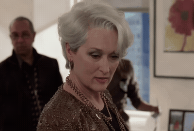 A Woman With Gray Hair And A Necklace Looks Down GIF