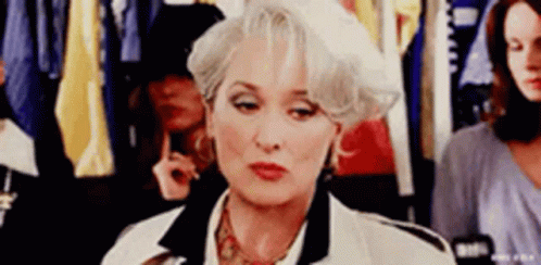 A Woman With Gray Hair And A White Hat Is Sitting In A Dressing Room . GIF