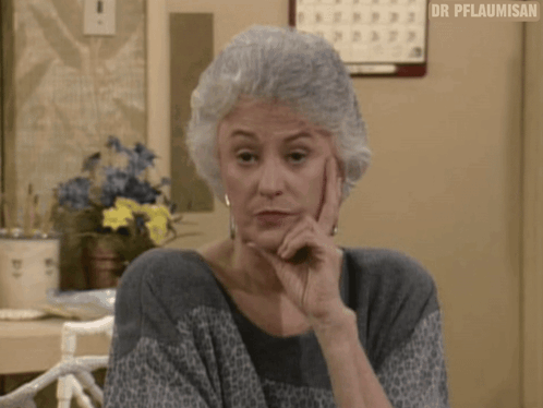 A Woman With Gray Hair Is Sitting At A Table With Her Hand On Her Chin And A Calendar On The Wall Behind Her . GIF