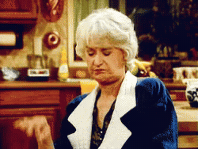 A Woman With Gray Hair Is Sitting In A Kitchen Making A Funny Face GIF