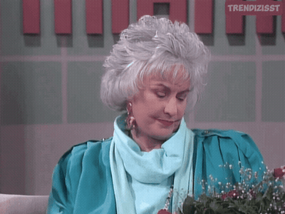 A Woman With Gray Hair Is Sitting In Front Of A Wall That Says Trendizsst GIF