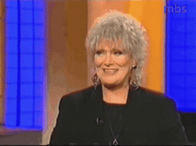 A Woman With Gray Hair Is Smiling In Front Of A Mbs Sign GIF