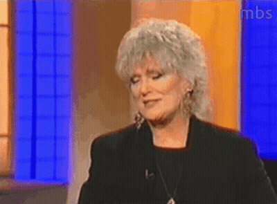 A Woman With Gray Hair Is Standing In Front Of A Blue Wall With Mbs Written On The Bottom GIF