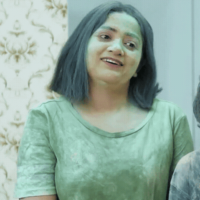 A Woman With Green Hair And A Green Shirt Is Smiling And Looking At The Camera . GIF