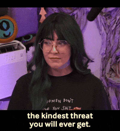 A Woman With Green Hair And Glasses Is Wearing A Black Shirt That Says Women Don T One You Shit GIF