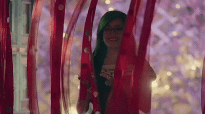 A Woman With Green Hair Is Standing Behind A Red Curtain . GIF