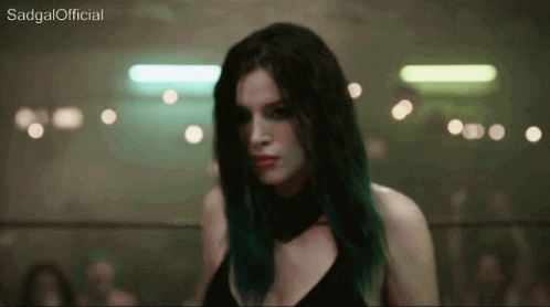 A Woman With Green Hair Is Standing In A Dark Room With Sadgal Official Written On The Bottom Of The Screen GIF
