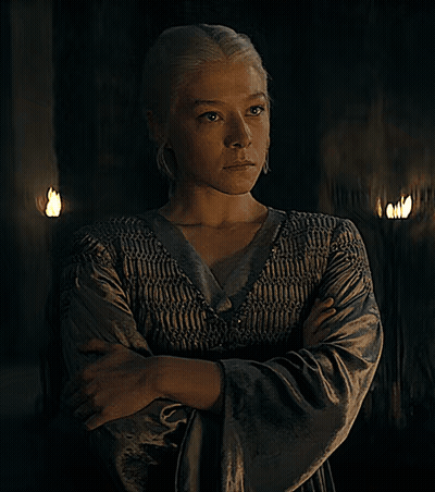 A Woman With Her Arms Crossed And Her Eyes Closed Stands In A Dark Room GIF