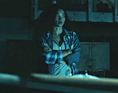A Woman With Her Arms Crossed Is Standing In A Dark Room . GIF