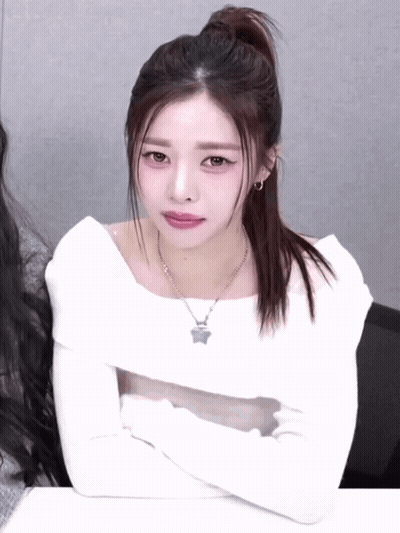 A Woman With Her Arms Crossed Wearing A White Top And A Necklace With A Star On It GIF