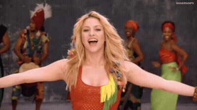 A Woman With Her Arms Outstretched In Front Of A Group Of People With Shakiragifs On The Bottom Right GIF