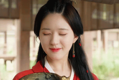 A Woman With Her Eyes Closed Is Wearing A Red Top And Earrings GIF
