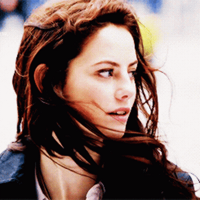 A Woman With Her Hair Blowing In The Wind Looks At The Camera GIF