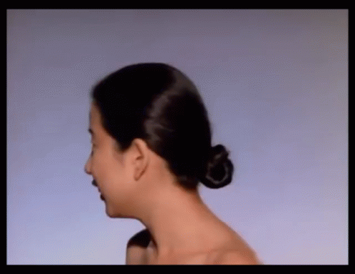 A Woman With Her Hair In A Bun Is Looking At Something GIF