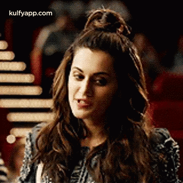 A Woman With Her Hair In A Bun Is Making A Funny Face And Looking At The Camera . GIF