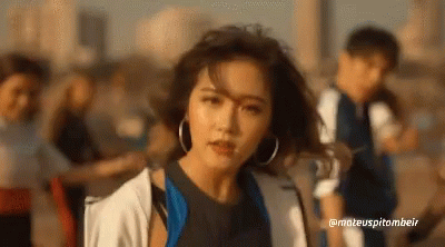 A Woman With Hoop Earrings Is Standing In Front Of A Group Of People .. GIF