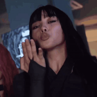 A Woman With Long Black Hair And Bangs Is Blowing A Kiss . GIF