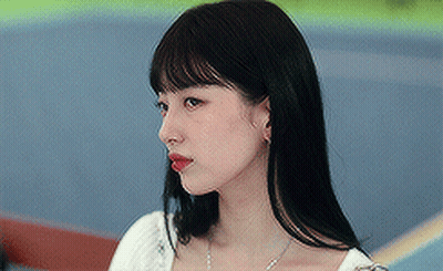 A Woman With Long Black Hair And Red Lipstick Is Wearing A White Top And A Necklace . GIF