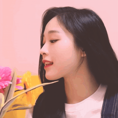 A Woman With Long Black Hair Is Holding A Flower In Her Hand GIF