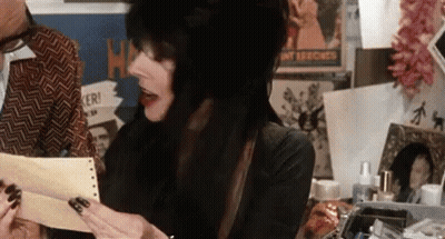 A Woman With Long Black Hair Is Holding A Piece Of Paper In Front Of A Man . GIF