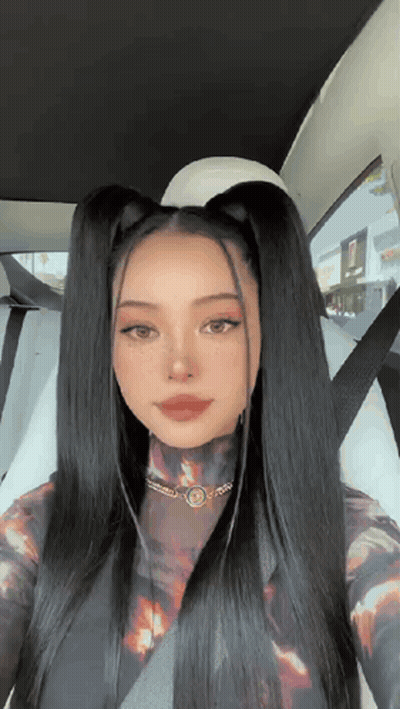 A Woman With Long Black Hair Is Sitting In A Car With A Seat Belt On . GIF