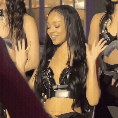 A Woman With Long Black Hair Is Sitting In A Chair And Waving Her Hand GIF