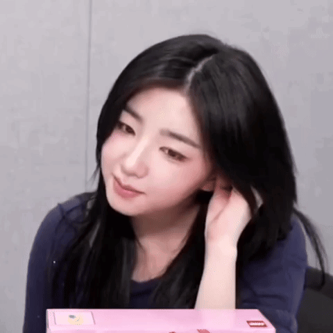A Woman With Long Black Hair Is Sitting In Front Of A Pink Box And Holding Her Hair . GIF