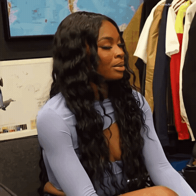 A Woman With Long Black Hair Is Sitting In Front Of A Wall With A Map On It GIF