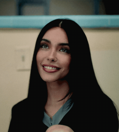 A Woman With Long Black Hair Is Smiling And Looking At The Camera GIF