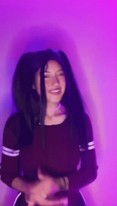 A Woman With Long Black Hair Is Standing In Front Of A Purple Wall . GIF