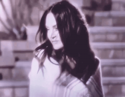 A Woman With Long Black Hair Is Standing In Front Of A Staircase . GIF
