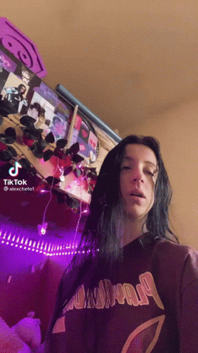 A Woman With Long Black Hair Is Standing In Front Of A Wall With Purple Lights . GIF