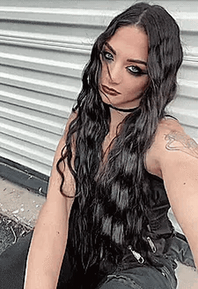 A Woman With Long Black Hair Is Taking A Selfie In Front Of A Wall . GIF
