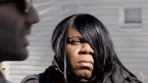 A Woman With Long Black Hair Is Talking To A Man In Front Of A House . GIF