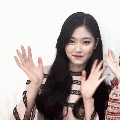 A Woman With Long Black Hair Is Waving Her Hands At The Camera . GIF