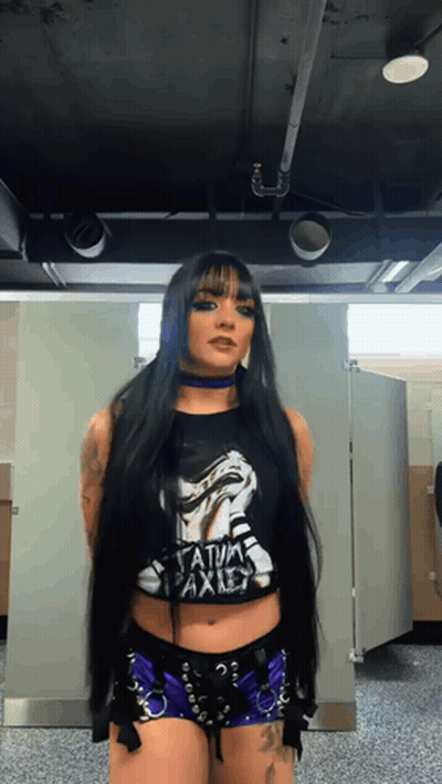 A Woman With Long Black Hair Is Wearing A Black Shirt That Says " Satanic Axis " GIF