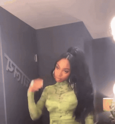 A Woman With Long Black Hair Is Wearing A Green Dress And A Ponytail . GIF