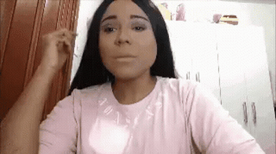 A Woman With Long Black Hair Is Wearing A Pink Shirt And Applying Makeup To Her Face . GIF