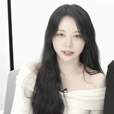 A Woman With Long Black Hair Is Wearing A White Off The Shoulder Sweater And Necklace . GIF