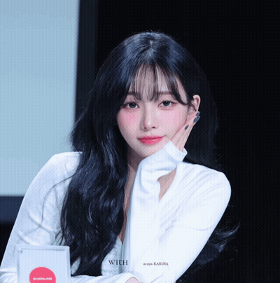 A Woman With Long Black Hair Is Wearing A White Shirt That Says Karina GIF