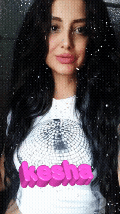 A Woman With Long Black Hair Is Wearing A White Shirt With The Word Kesha On It GIF