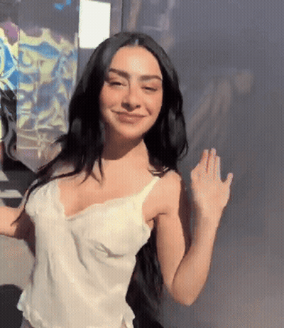 A Woman With Long Black Hair Is Wearing A White Tank Top And Smiling GIF