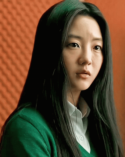 A Woman With Long Black Hair Wearing A Green Sweater And White Shirt GIF