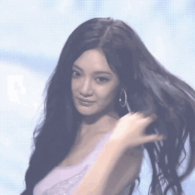 A Woman With Long Black Hair Wearing Hoop Earrings Looks At The Camera GIF
