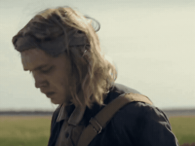 A Woman With Long Blonde Hair And A Brown Backpack Looks Down GIF