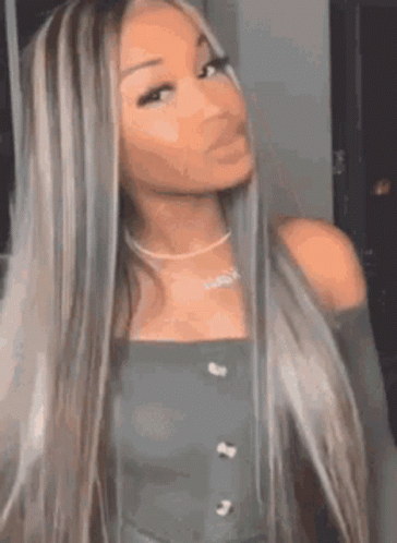 A Woman With Long Blonde Hair And A Necklace Is Standing In Front Of A Mirror And Looking At The Camera . GIF