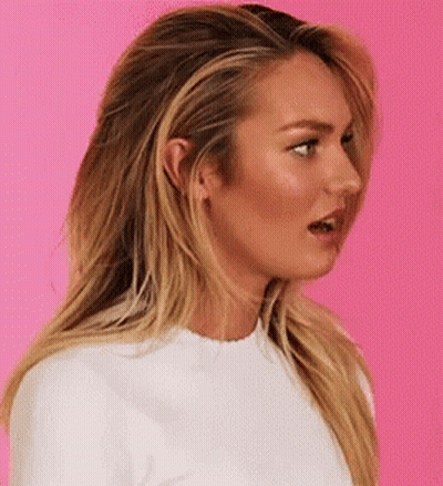 A Woman With Long Blonde Hair And A White Shirt Is Making A Funny Face . GIF