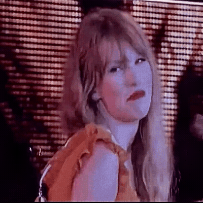 A Woman With Long Blonde Hair And Red Lips Is Making A Funny Face In Front Of A Curtain . GIF