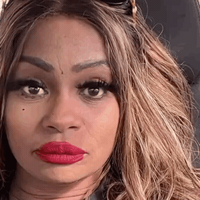 A Woman With Long Blonde Hair And Red Lipstick Is Sitting In A Car And Making A Funny Face . GIF
