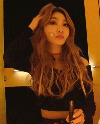 A Woman With Long Blonde Hair Is Holding A Microphone And Adjusting Her Hair GIF